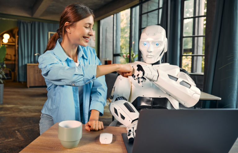 Woman and robot using a laptop bumping fists.