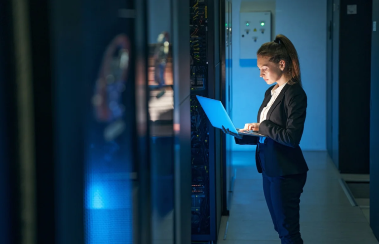 Woman working on a laptop inside a data center.